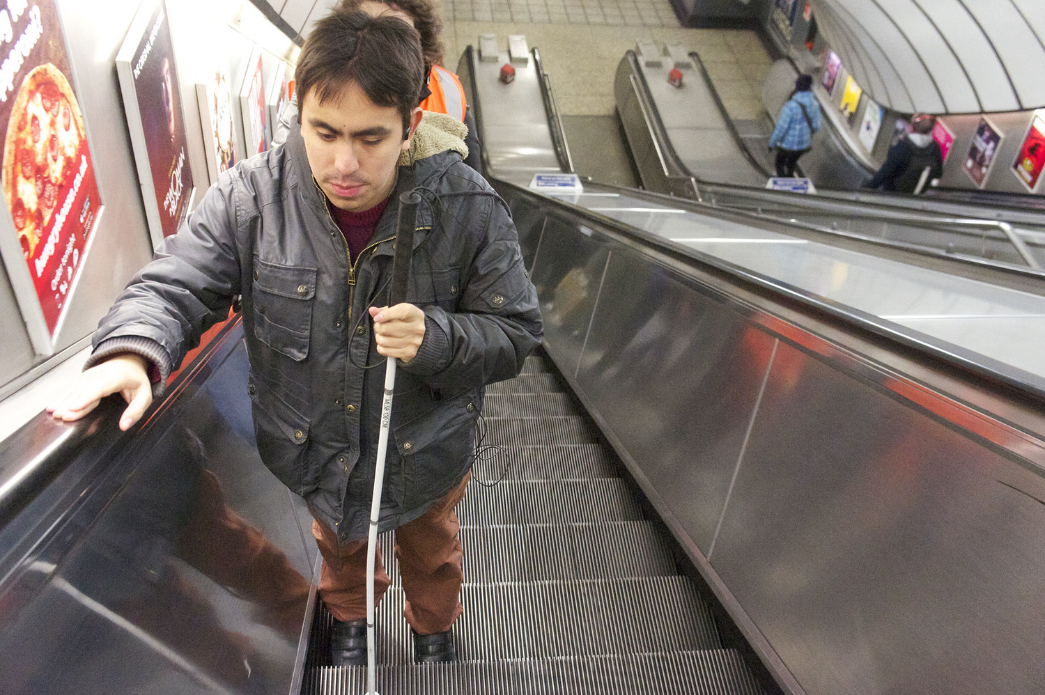A vision impaired person going up the escalator in a tube station while trying Wayfindr